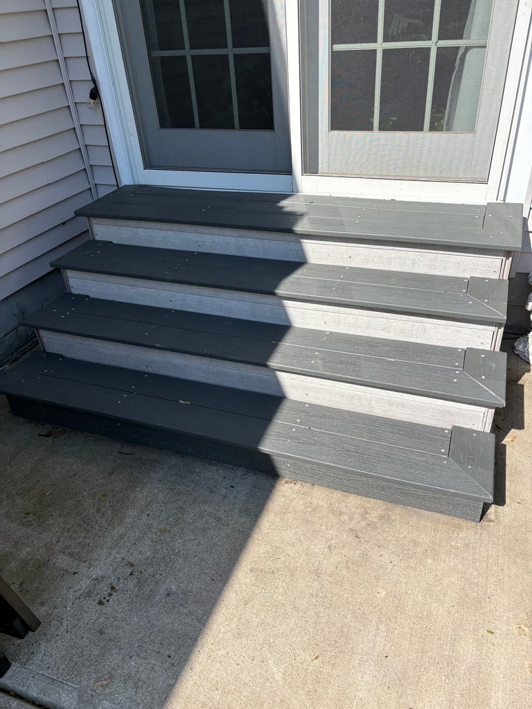 Exterior wooden deck stairs with dark gray treads and light gray risers leading to a white door with glass panels