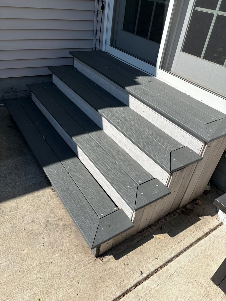 Gray composite deck steps leading to a glass sliding door on a house exterior with vinyl siding